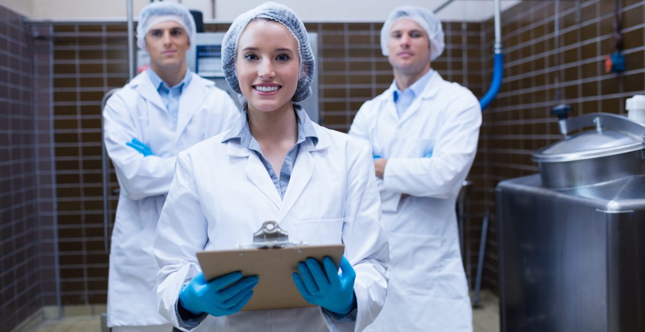 Girl holding a clipboard with these colleagues behind her in the factory
